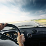 Driver's hands on a steering wheel of a car and blue sky with bl