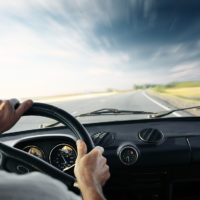 Driver's hands on a steering wheel of a car and blue sky with bl