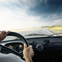 Driver's hands on a steering wheel of a car and blue sky with bl Driver's hands on a steering wheel of a car and blue sky with bl