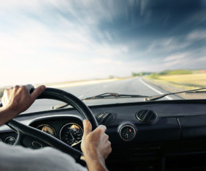 Driver's hands on a steering wheel of a car and blue sky with bl